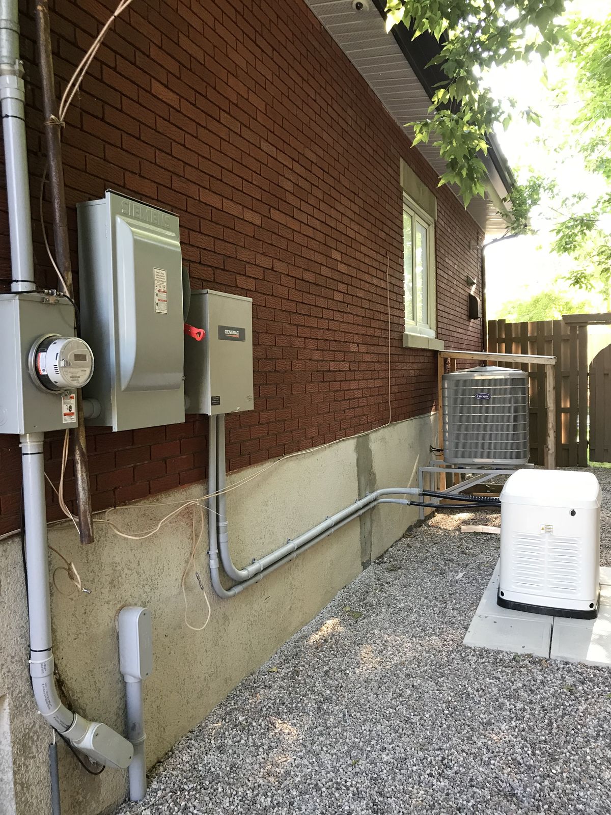 Une génératrice de secours installée à côté d'une maison de brique, raccordée à un commutateur de transfert avec conduits soignés