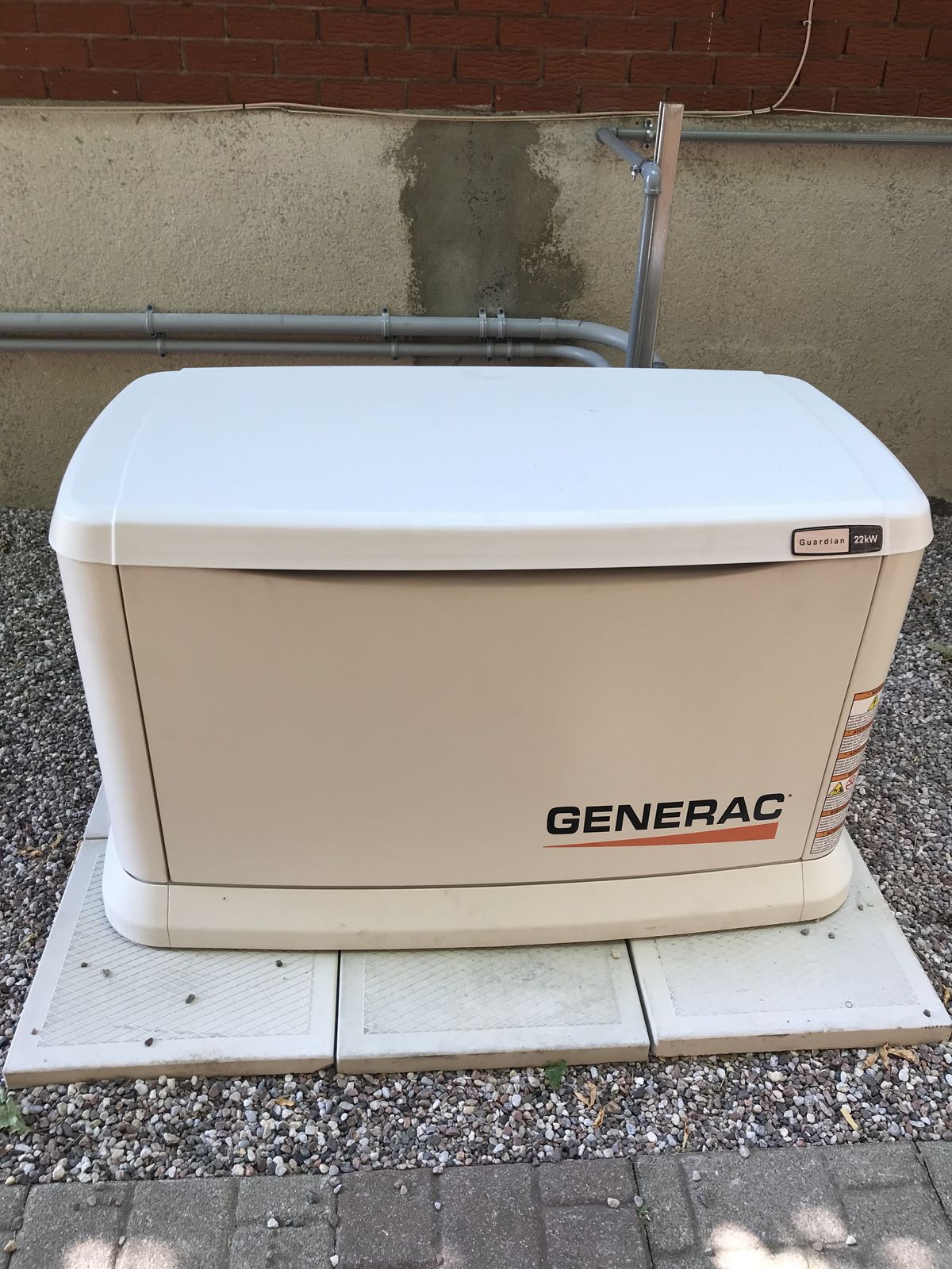 Une génératrice de secours installée sur une base de pavé à côté d'une maison